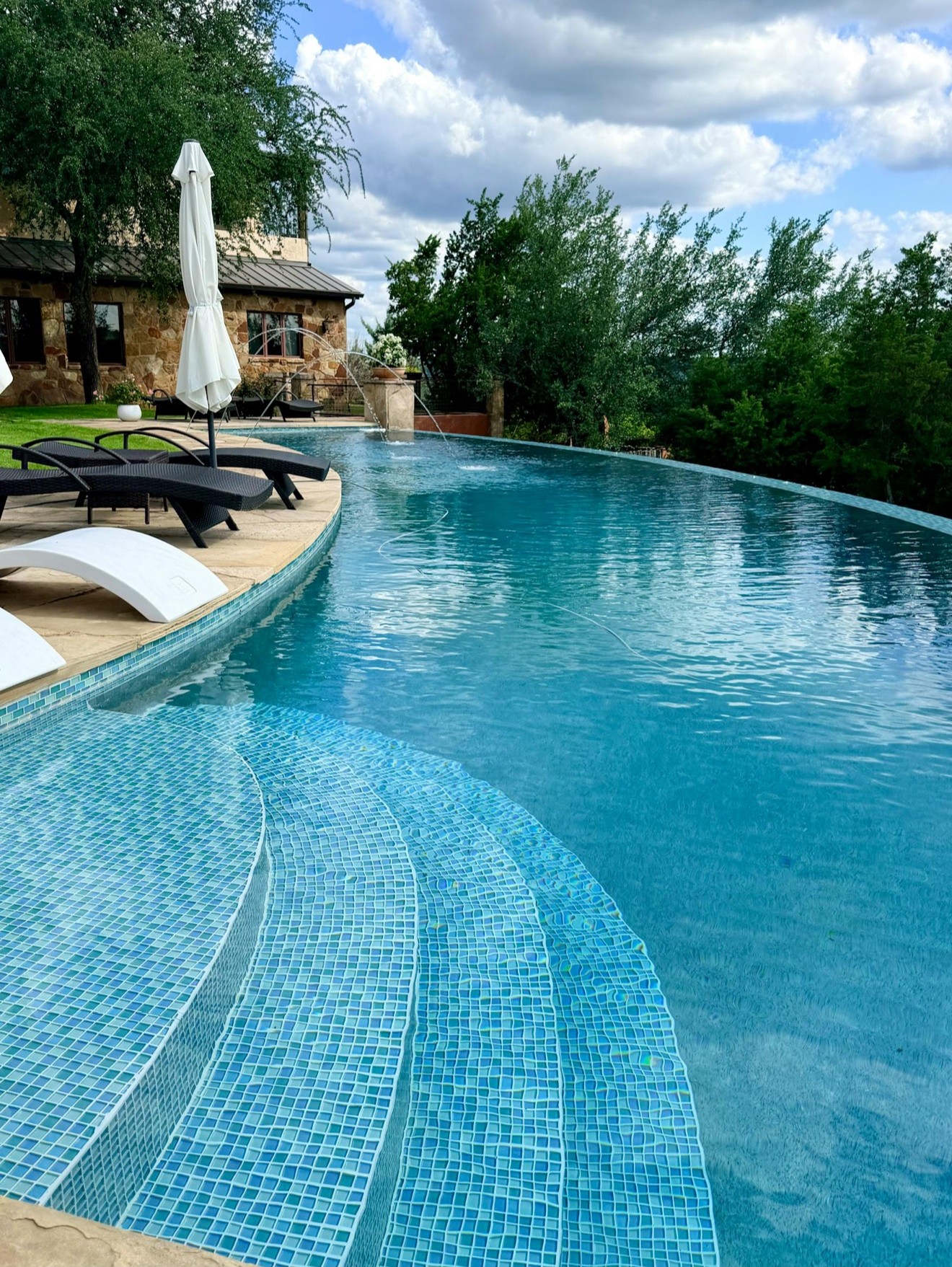 SORAE Estate curved infinity pool with mosaic steps, lounge chairs, and stone villa